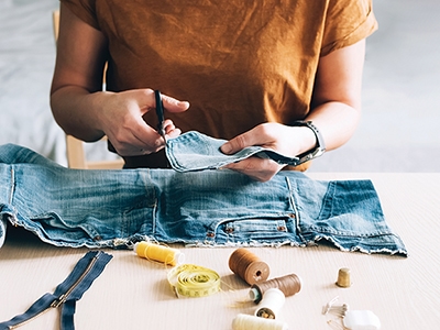 Woman repairs sews reuses fabric from old denim clothes economical reuse