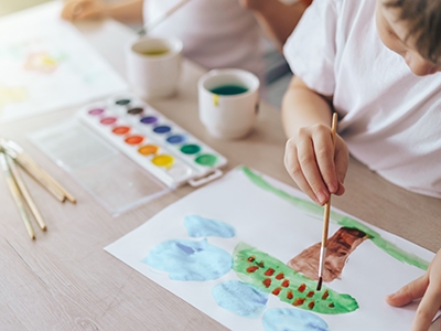 Children paint green grass with a tree and blue clouds.