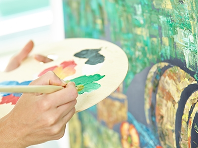 Human hands holding palette and paintbrush and preparing to make finishing touches